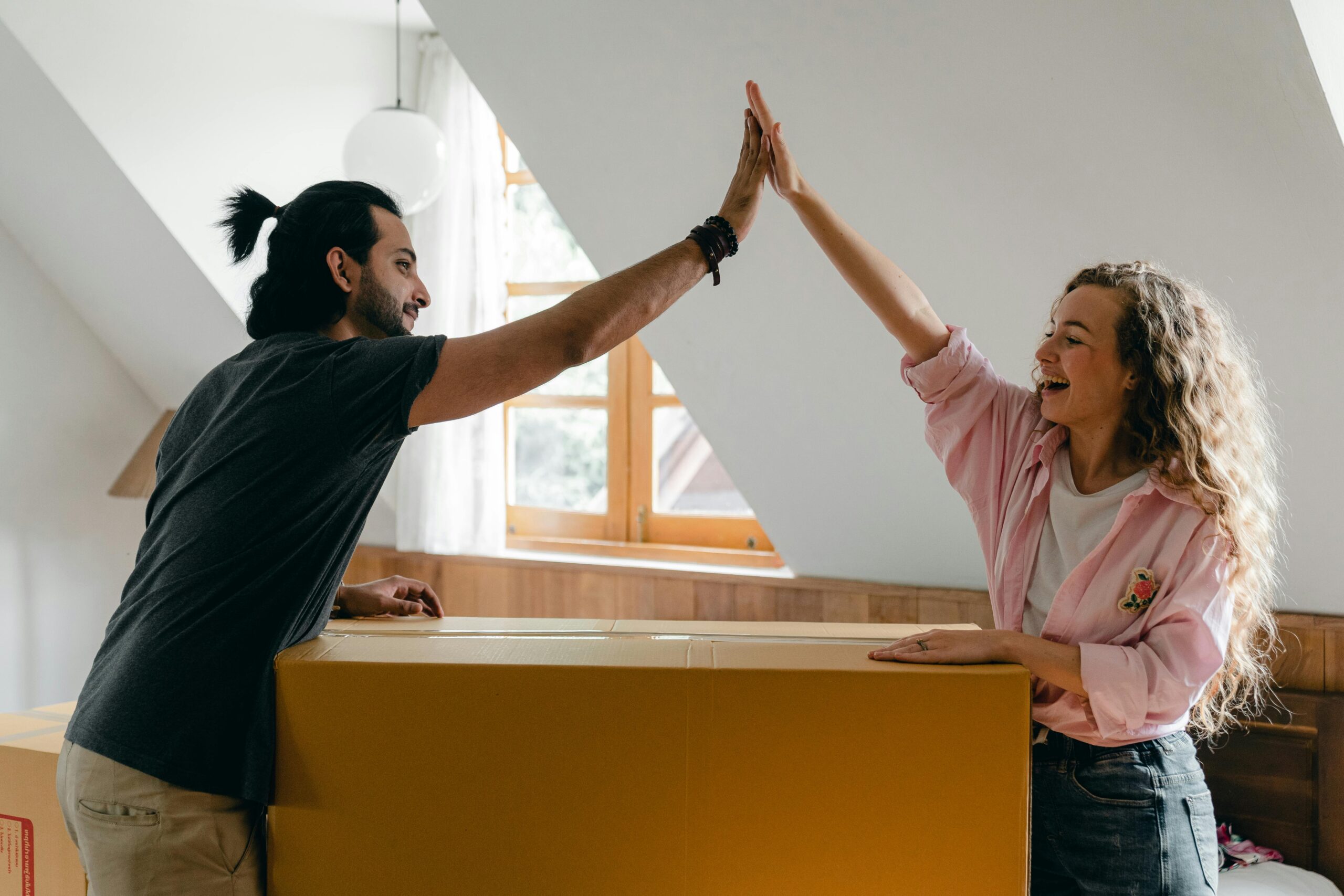 Young couple high-fiving in their new home, happily surrounded by moving boxes.